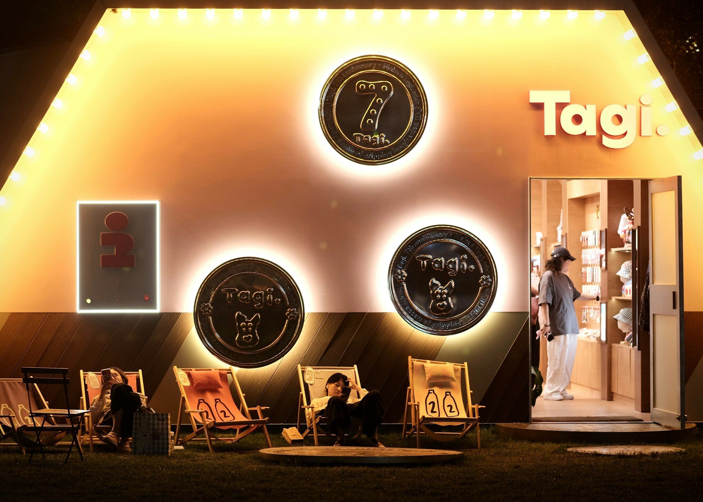 Guests relaxing outside a warmly lit pop-up with circular wall signs