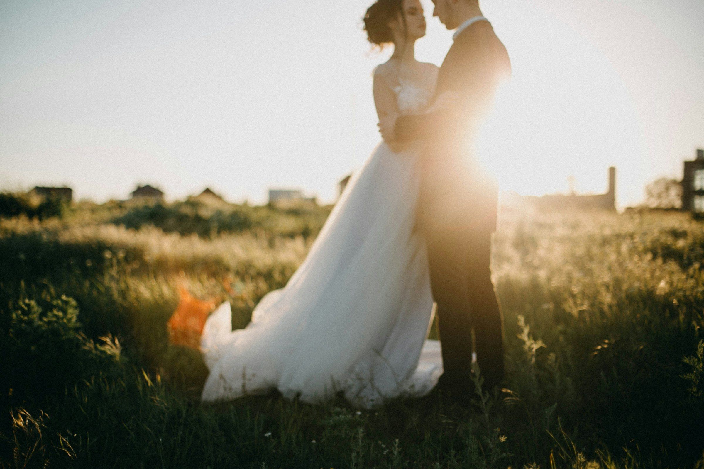 A couple embracing in a meadow as the sun sets behind them