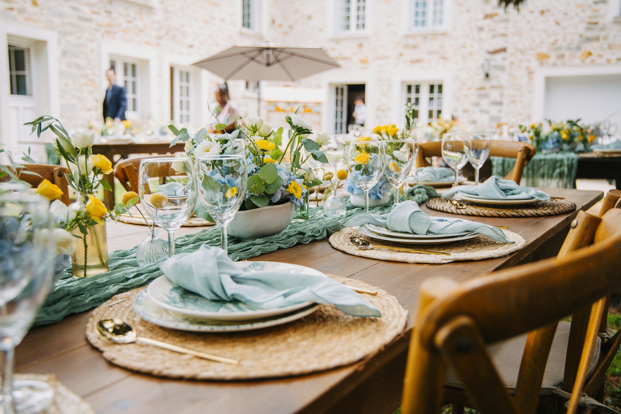 An outdoor table set with blue linens and yellow floral arrangements