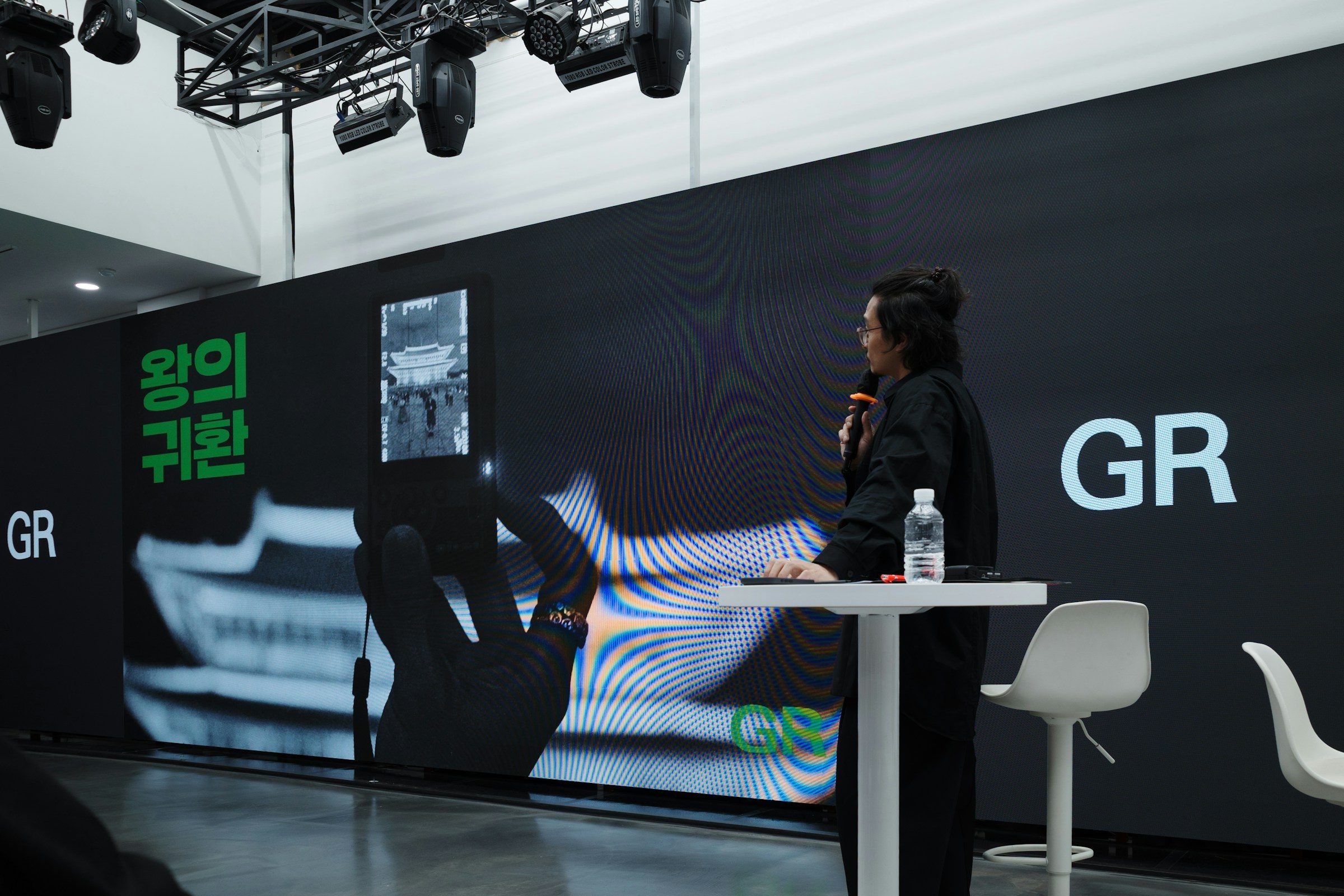 A speaker presenting beside a large illuminated screen