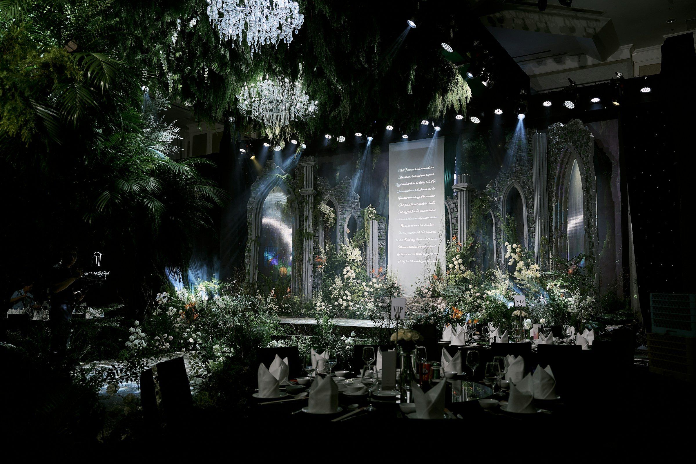A candlelit gala stage dressed with white florals, crystal chandeliers and dramatic lighting