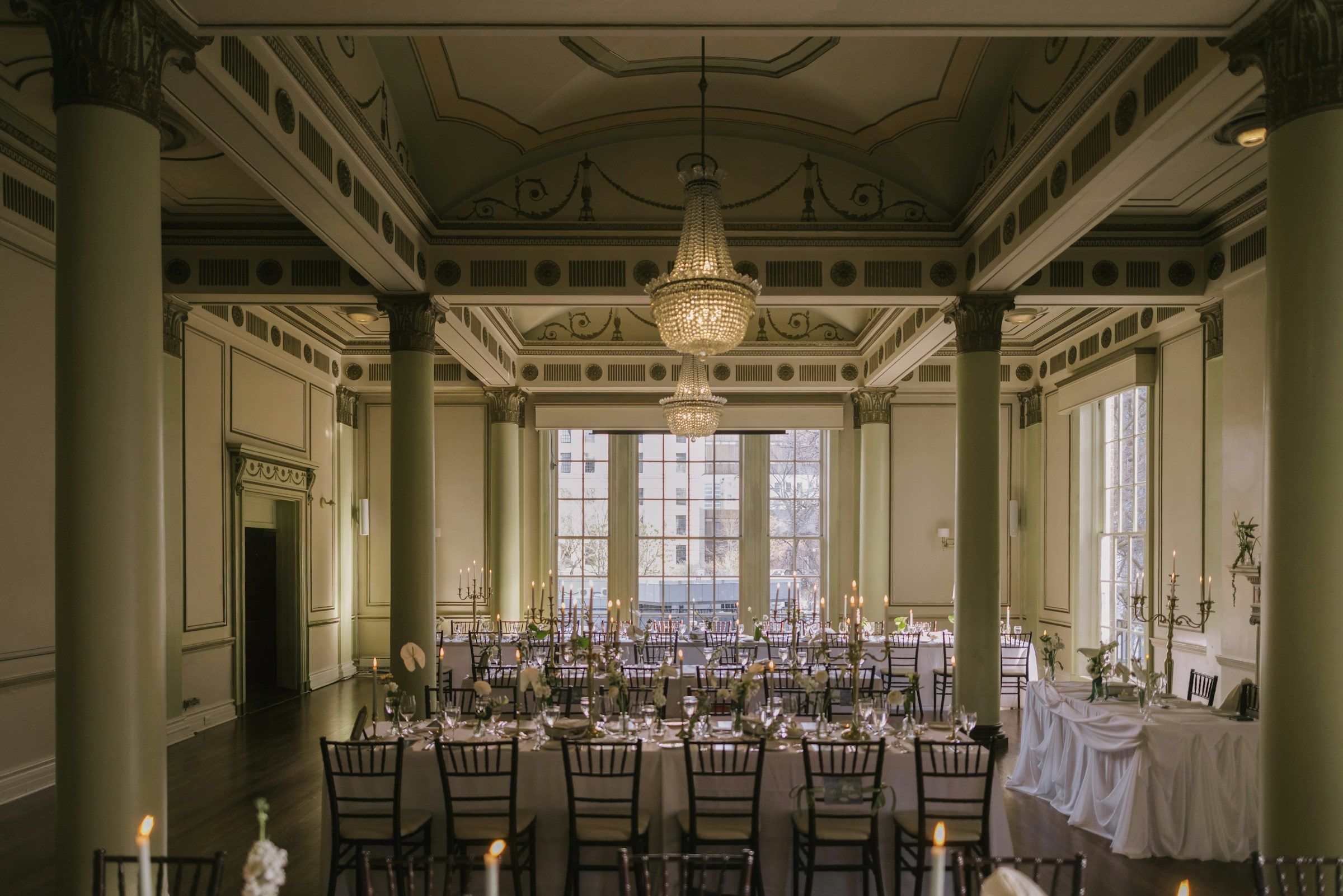 An elegant ballroom with tall columns, chandeliers and long tables